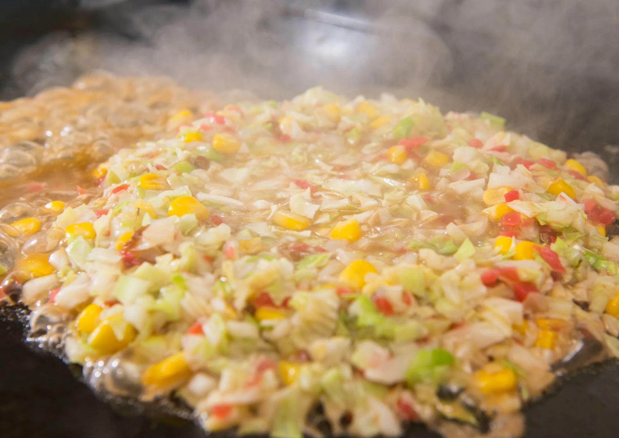 Monjayaki cooking on the griddle with cabbage and corn